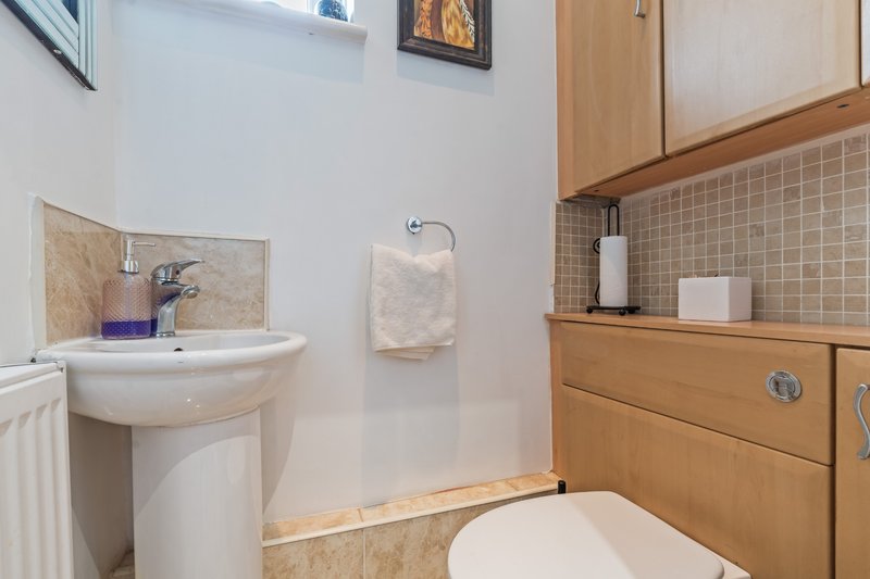 Compact bathroom with pedestal sink, toilet, wooden cabinetry and beige tile backsplash
