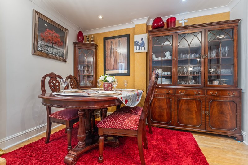 Formal dining room with round wooden table, red chairs, large display cabinet and artwork on walls
