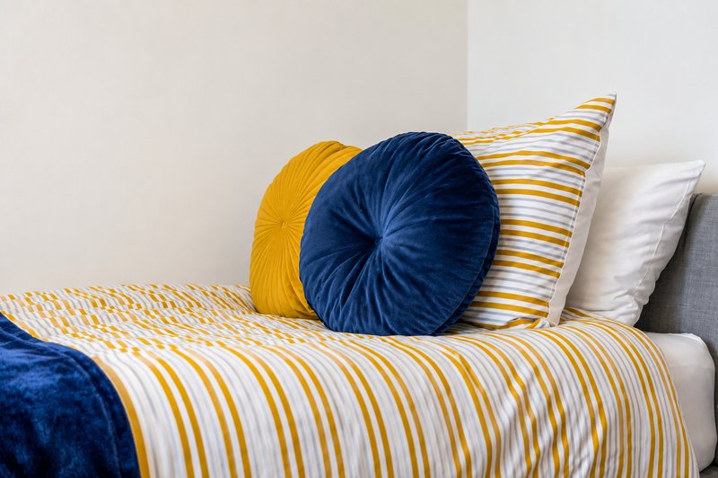 Bed with yellow and blue striped bedding, decorative round cushions and white pillow