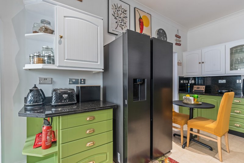 Modern kitchen with lime-green cabinetry, black countertops, stainless steel refrigerator and dining area