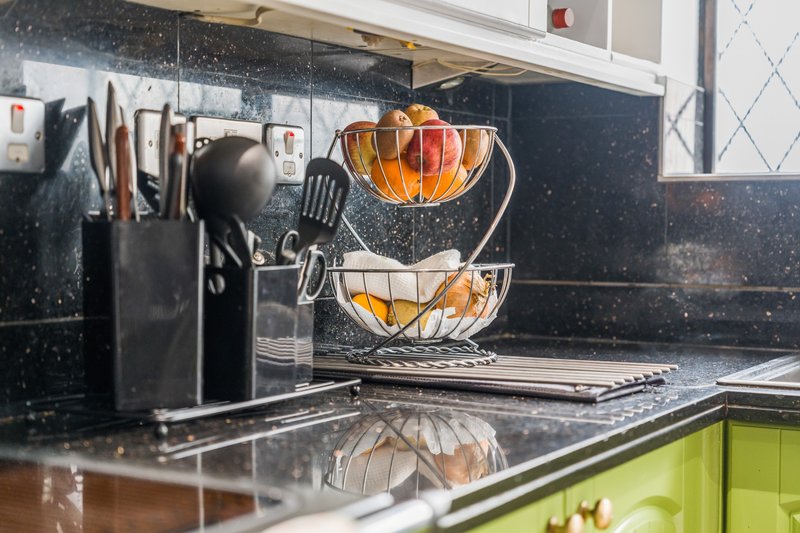 Modern kitchen counter with black splashback, fruit basket, utensil holder and lime green cabinet doors