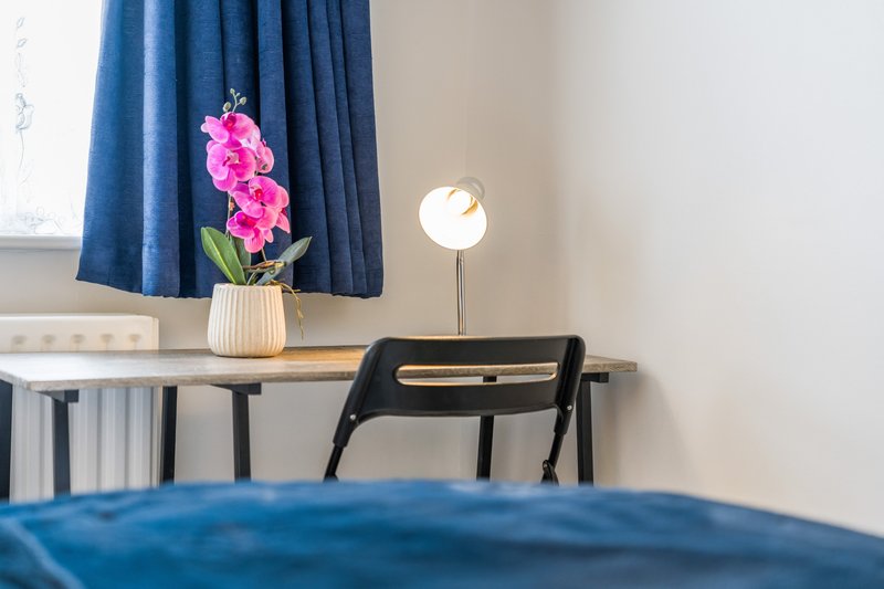 Bedroom with blue curtains, desk with pink flowers, lamp and black chair