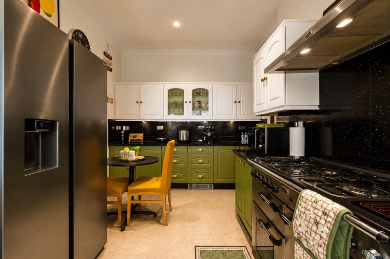 Modern kitchen with black countertops, green cabinetry, stainless steel appliances and yellow chair