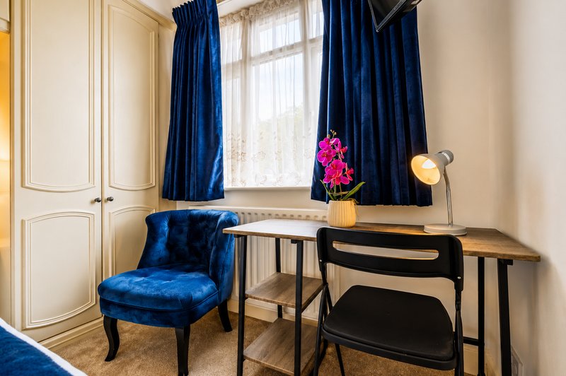Bedroom alcove with blue velvet chair, desk, wooden floor and window with blue curtains