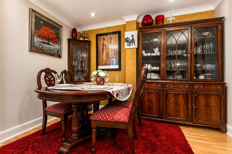 Formal dining room with round wooden table, ornate chairs, red rug, and glass-fronted display cabinets
