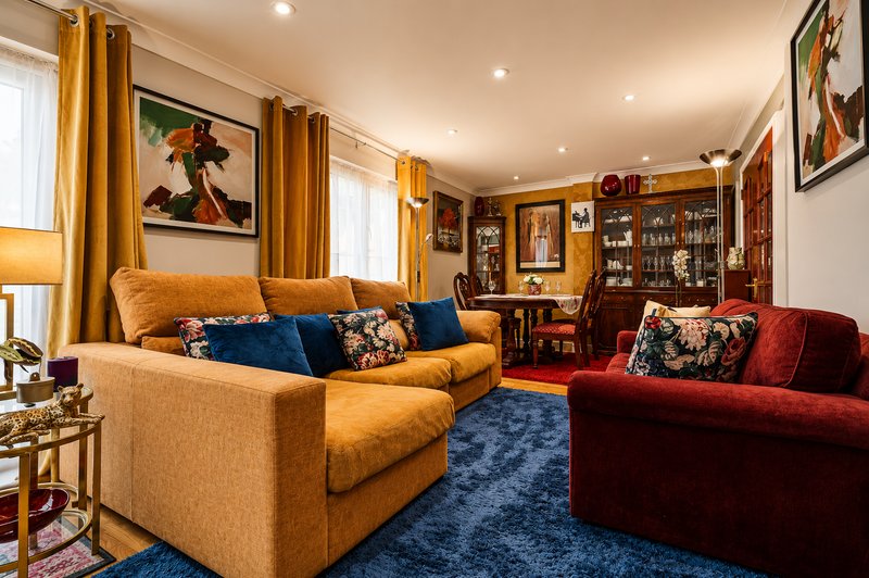Spacious living room with gold and red sofas, blue rug, wooden shelving, and framed artwork