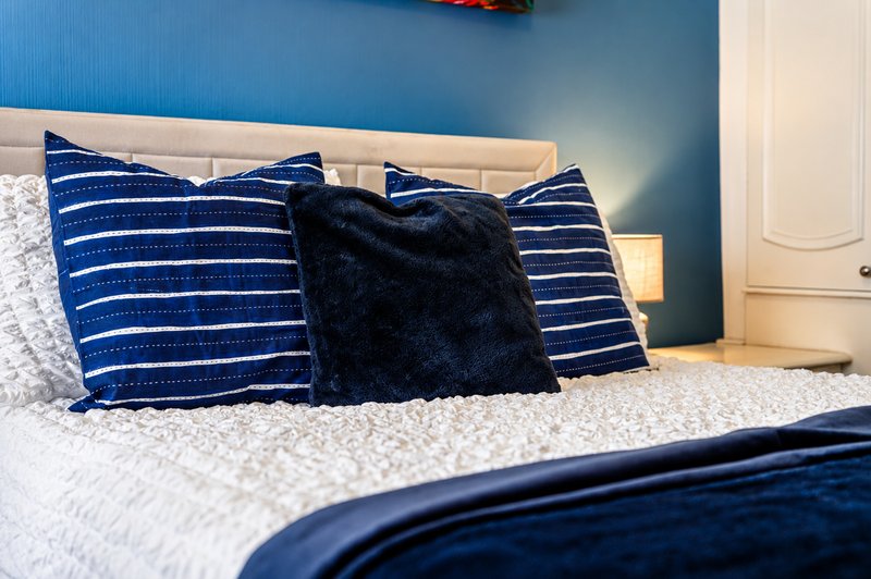 Bedroom with blue accent wall, bed dressed with striped pillows and black cushion