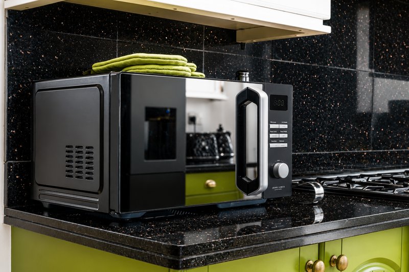 Modern kitchen counter with black speckled countertop, lime-green cabinet, and black microwave and kettle appliances
