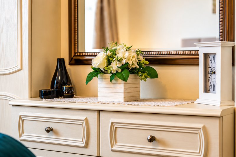 Cream dresser with mirror, decorated with flower arrangement, wine bottle, and candles