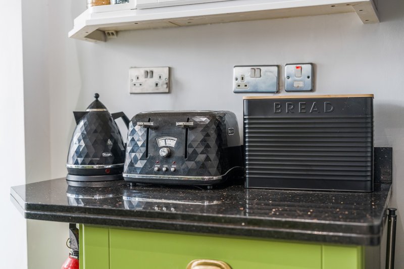 Kitchen counter with black kettle, toaster, bread bin and wall-mounted electrical outlets