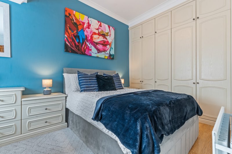 Bedroom with blue accent wall, double bed with navy bedding, white furniture and colorful abstract artwork