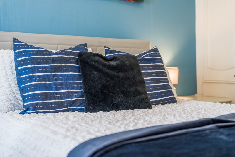 Bedroom with double bed, blue striped pillows, black fur cushion and white bedding