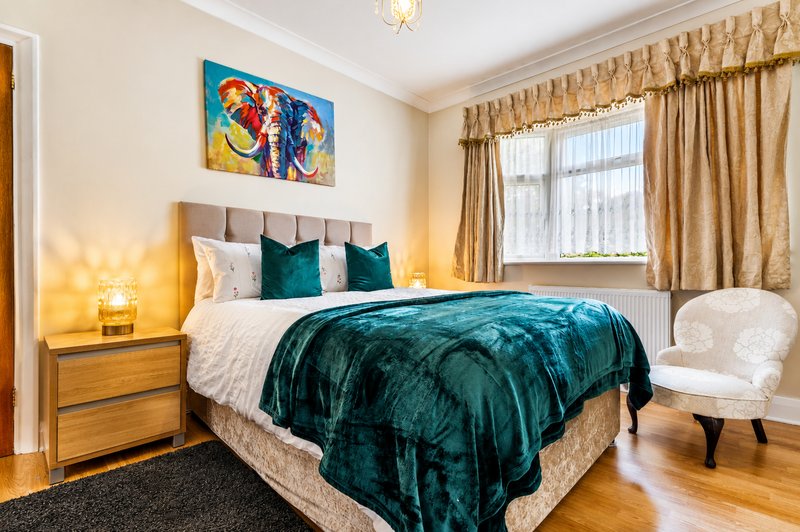 Bright bedroom with double bed, teal bedding, wooden nightstand, upholstered headboard, armchair and artwork