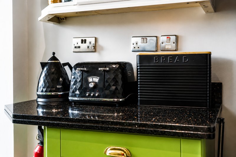 Kitchen counter with black speckled worktop, lime-green cabinet, electric kettle, toaster, bread bin and wall outlets