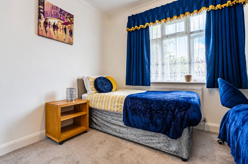 Bedroom with single bed, blue velvet bedspread, wooden nightstand and blue curtains