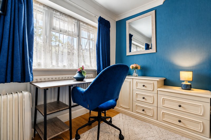 Modern bedroom with blue accent wall, desk with chair, dresser, and window with blue curtains