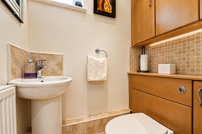 Bathroom with pedestal sink, toilet, wooden cabinetry and tiled walls