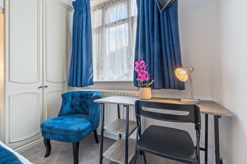 Bright bedroom corner with blue velvet chair, desk, window with blue curtains and flowers