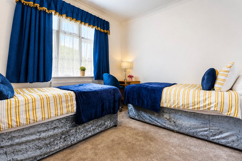 Bright bedroom with three single beds, blue curtains, and striped bedding