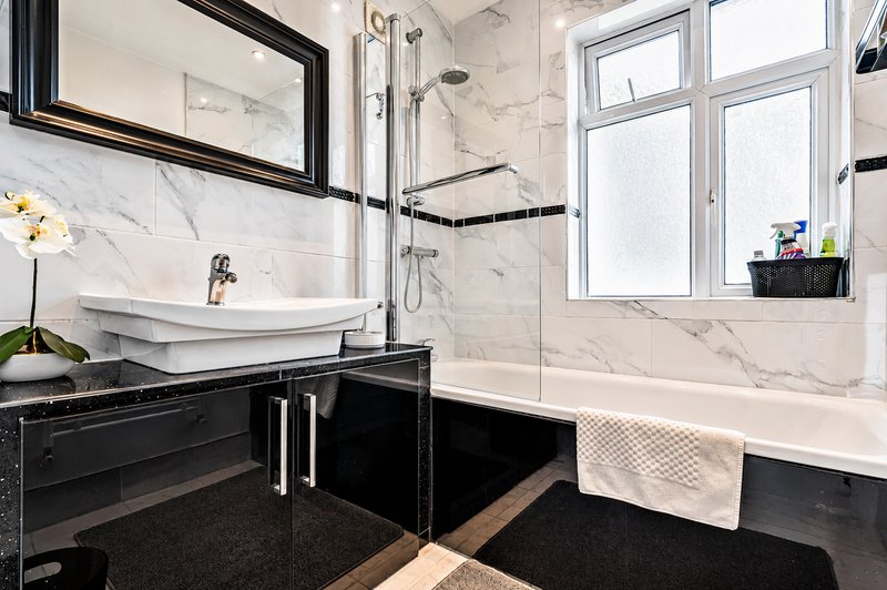Modern bathroom with marble tiles, black vanity, vessel sink, walk-in shower and bathtub