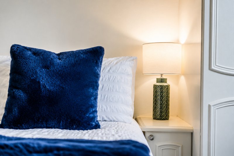 Bedroom with blue velvet cushion, white pillow, bedside lamp and wooden nightstand