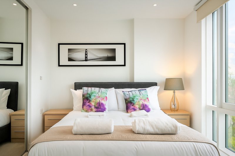 Bright modern bedroom with double bed, wooden nightstands, floral cushions and framed wall art