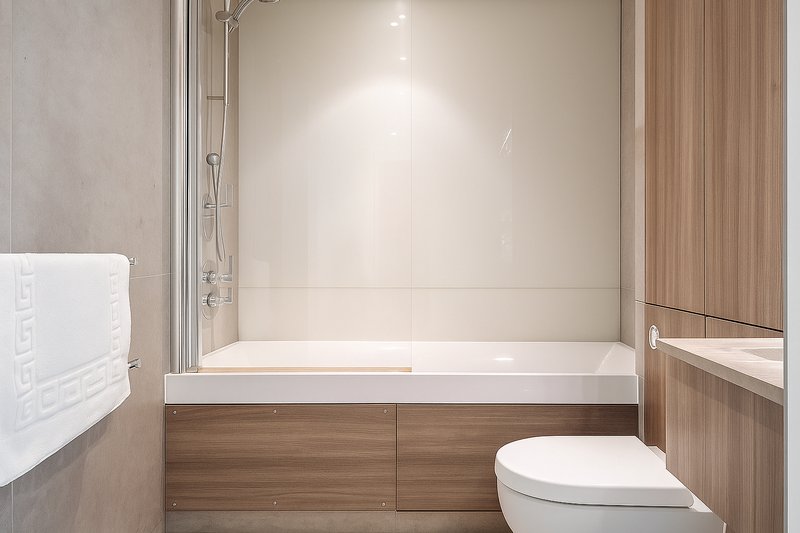 Modern bathroom with white bathtub, toilet, and wooden vanity cabinetry