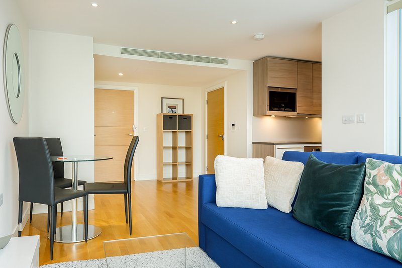Modern open-plan living space with blue sofa, dining table, wooden flooring and built-in storage