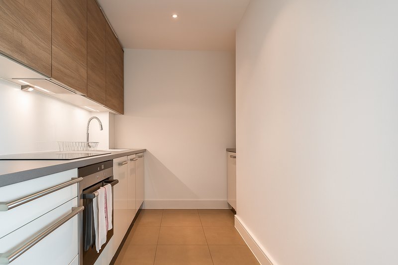 Modern galley kitchen with white cabinetry, wooden upper units, stainless steel appliances and terracotta flooring