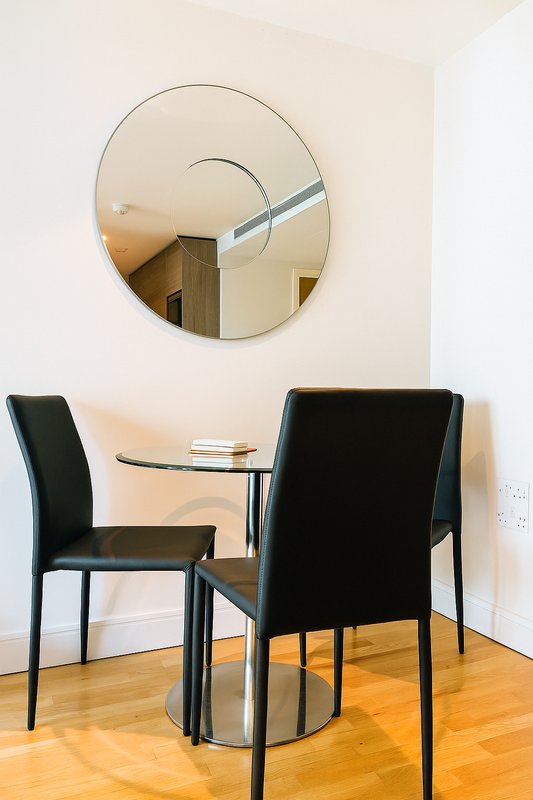 Dining area with two black chairs, round glass table, and circular wall mirror