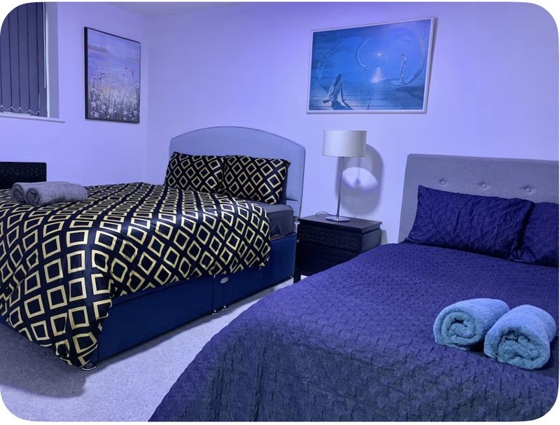 Bedroom with two beds, geometric bedding, wall art, and rolled towels on bed