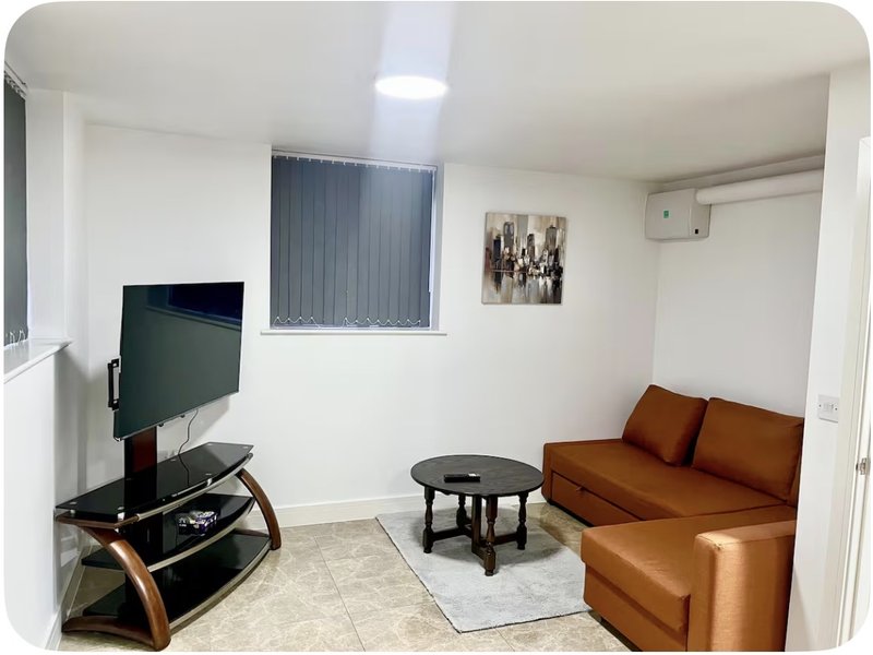 Living room with brown sofa, TV on stand, small round table, and window with vertical blinds