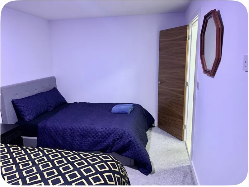 Compact bedroom with single bed, dark blue bedding, wooden door and wall mirror