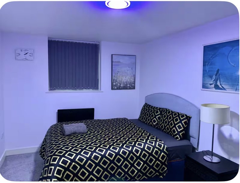 Bedroom with double bed, patterned bedding, window blinds, wall art and side lamp