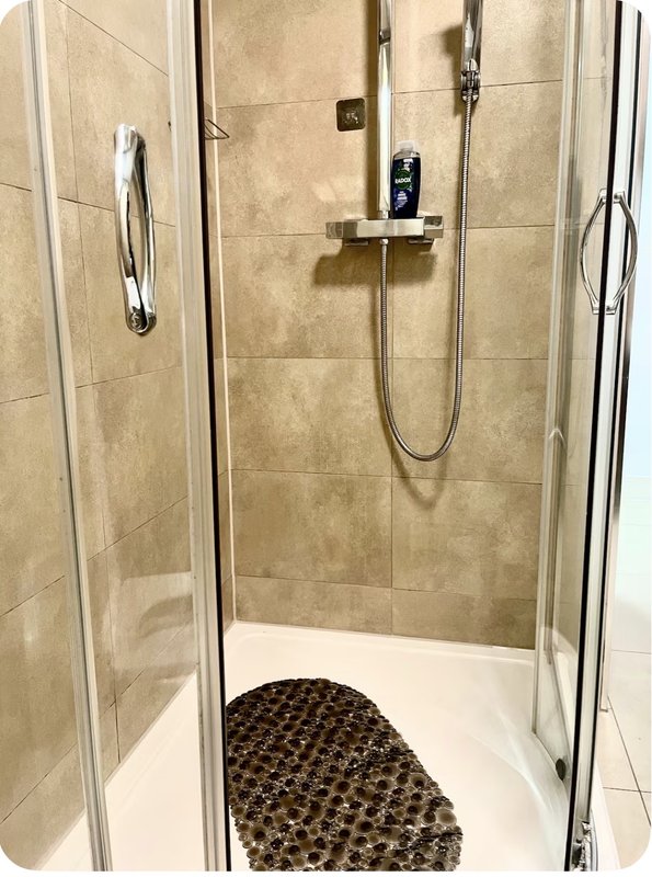 Modern walk-in shower with glass enclosure, beige tile walls and dark mat on floor