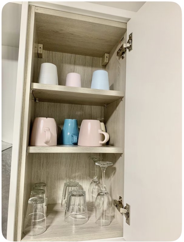 Open kitchen cabinet with mugs, cups and glassware neatly arranged on wooden shelves