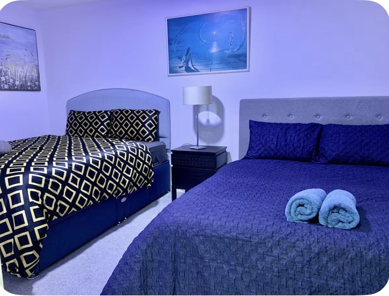 Bedroom with two beds, patterned bedding, rolled towels, framed artwork and side table