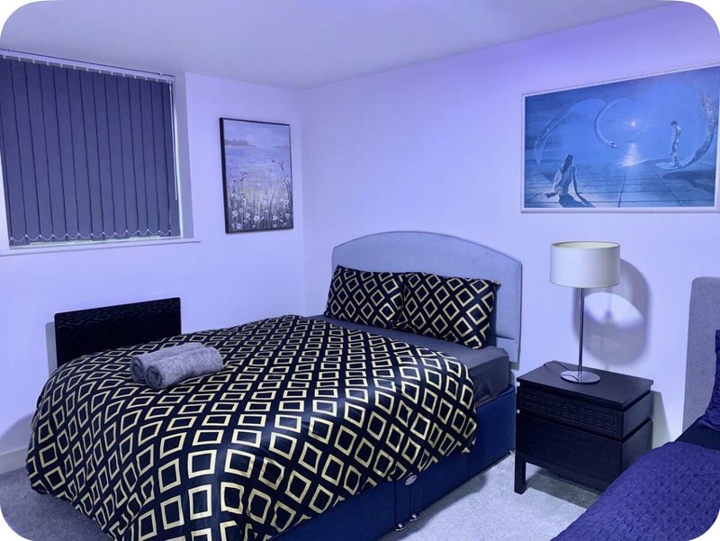 Bedroom with double bed, geometric patterned bedding, bedside lamp, and framed wall art