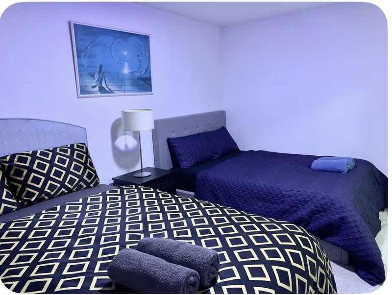 Bedroom with two beds, geometric patterned bedding, wall-mounted TV and white bedside table