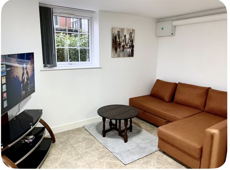 Living room with tan leather sectional sofa, round black coffee table, TV on stand, and window with curtains
