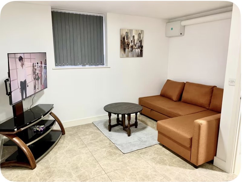 Modern living room with tan leather sofa, black coffee table, TV stand and window with blinds
