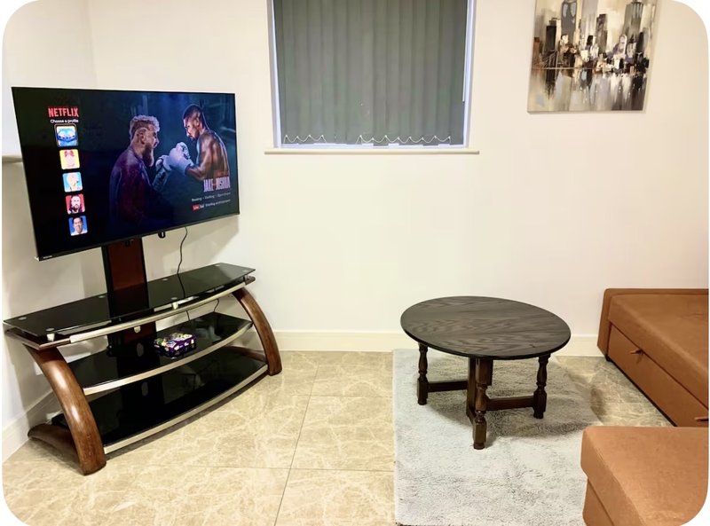 Living room with wall-mounted TV, wooden TV stand, round coffee table, and tan leather seating