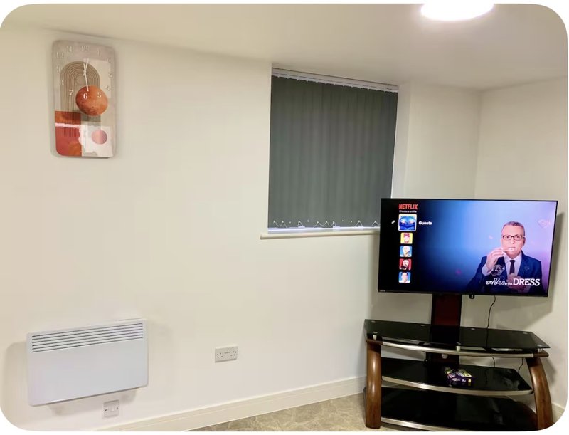 Furnished living room with TV on wall mount, electric heater, window with blinds and wall art