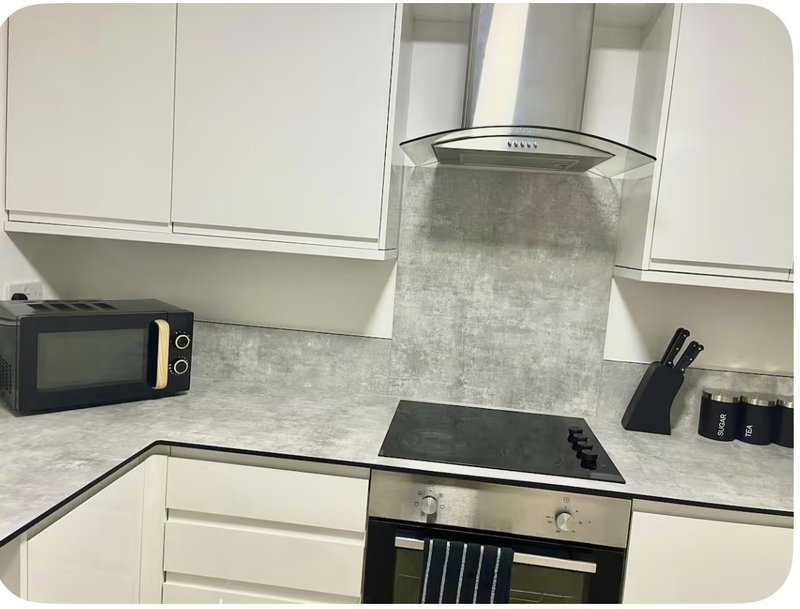 Modern kitchen with white cabinets, grey splashback, induction hob and stainless steel extractor hood