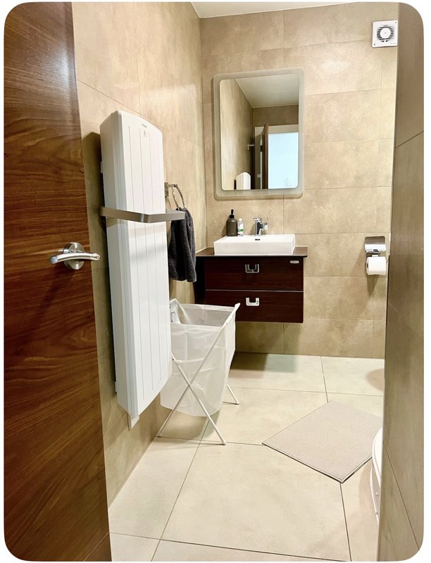 Modern bathroom with vanity sink, mirror, heated towel rail, and tiled flooring