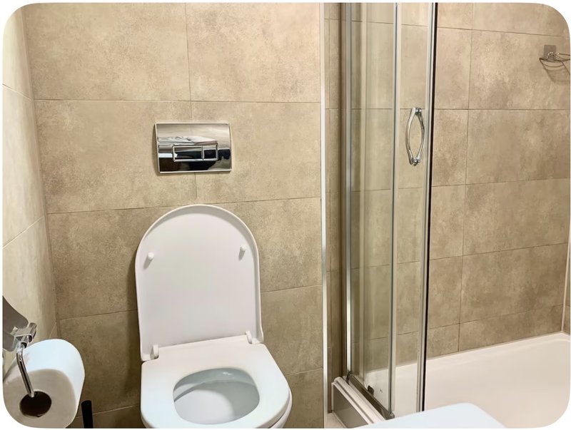 Bathroom with white toilet, tile walls, paper towel dispenser, and glass shower enclosure