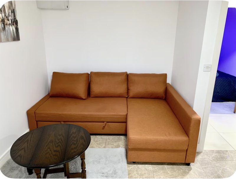 Living room with tan leather corner sofa, dark wooden side table, and white walls