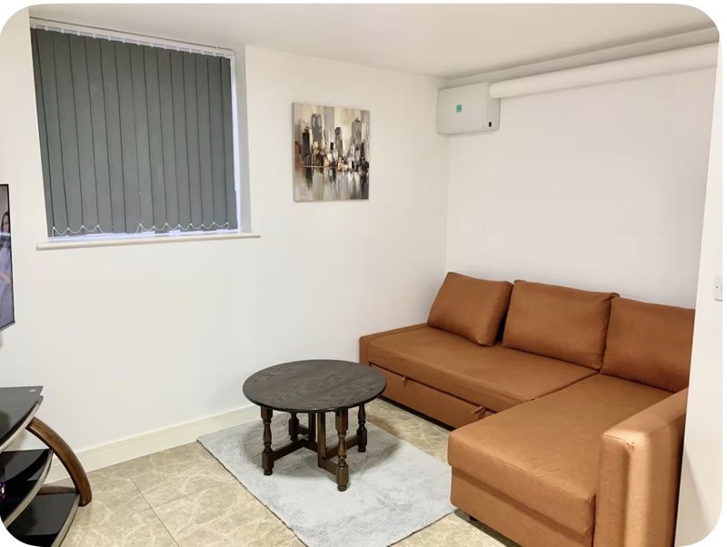 Living room with tan leather sectional sofa, round dark table, vertical blinds and wall art