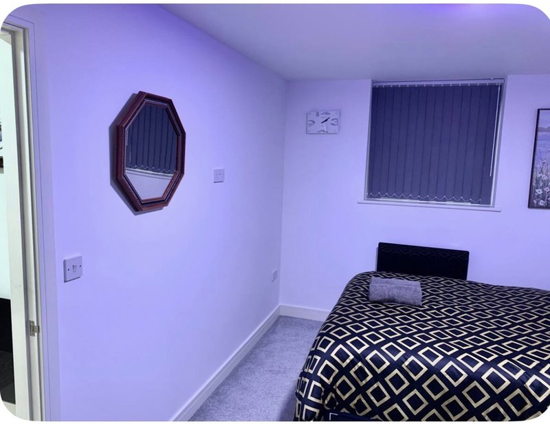 Modern bedroom with purple walls, double bed with geometric patterned duvet, octagonal mirror and vertical blinds