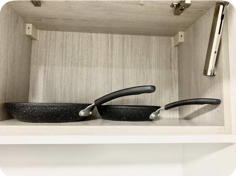 Kitchen cabinet shelf with two black non-stick frying pans and cooking utensils